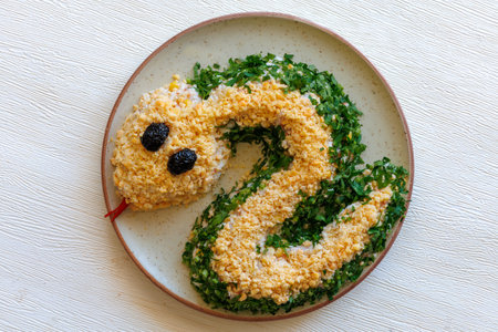 Salad with shrimps, egg, chicken, cheese and parsley in shape of green Snake as symbol of Chinese new year on a plate on a white table. Creative design for party. Top view.の写真素材