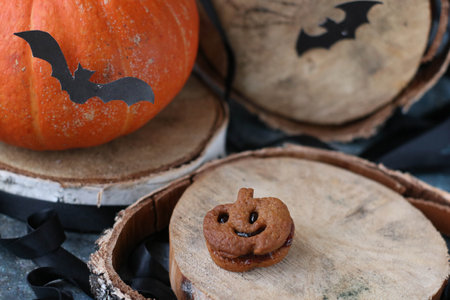 Pumkin cookies looking like Jack-o-lantern lying on wooden tray with orange pumpkin and black bats on backgroundの写真素材