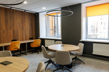 Empty working and meeting area in an open office. White round wooden table surrounded by chairs in gray and yellow colors. Big window backgroundの写真素材