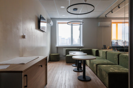 Empty rest area in an open office. White round wooden table surrounded by green sofa. Window on backgroundの写真素材