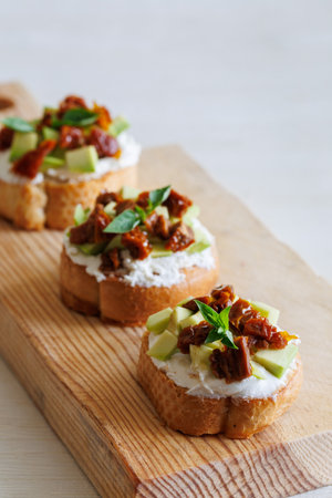 selective focus of italian bruschetta with dried tomatoes, avocado, cream cheese and herbs on wooden board, close up, verticalの写真素材