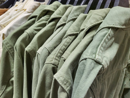 Dresses of monochrome green khaki colors hang on closing rack on wooden hangers. Close up full frame backgroundの写真素材