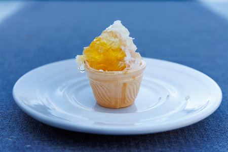 Close-up of honeycomb in a small waffle cone, placed on white plate against a blue background. Close upの写真素材