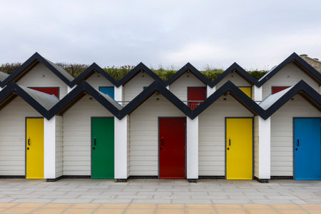White wooden beach huts with bright doors in spring in seafront with cloud sky in background in Swanage, UK. South coast of England, Dorset. No peopleの写真素材