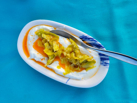 Appetizing dish features creamy yogurt topped with sliced pickled peppers and spicy oil. Served in white dish on vibrant blue surface, top view, close upの写真素材