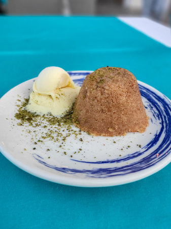 Semolina Halva turkish traditional dessert Irmik Helvasi with scoop of vanilla Ice Cream on white blue plate with crushed pistachios. Verticalの写真素材