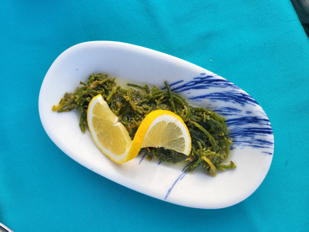Fresh seaweed salad garnished with lemon slices on a white plate, placed on a bright blue tablecloth. Top view, vegetarian healthy food conceptの写真素材