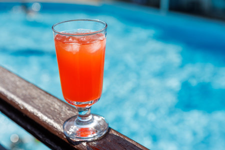 Vibrant red cocktail in glass with ice cubes on wooden poolside railing. summer holiday leisure and enjoyment by water conceptの写真素材