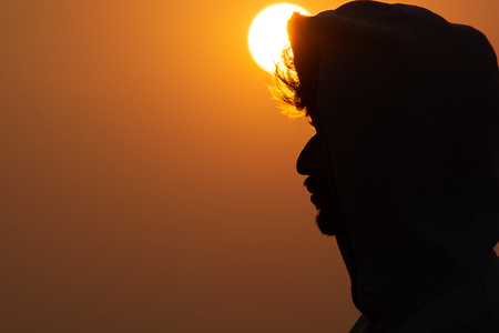 Close up of a person weared hoody standing above the mountain with sunset backgroundの写真素材