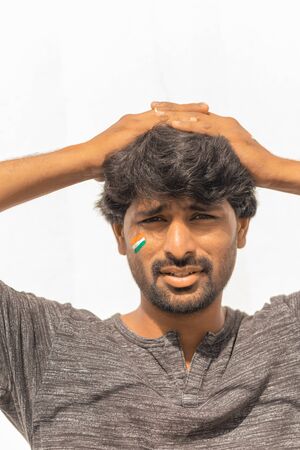 Portrait of curious or tense Young Indian male Cricket sports fan Painted Indian flag on his faceの写真素材
