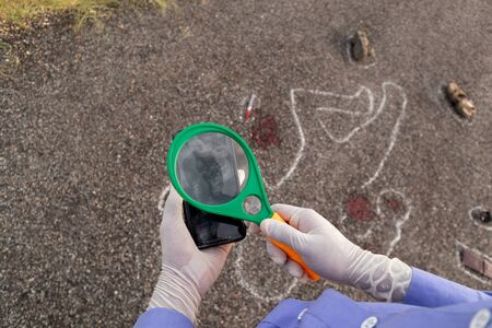 Detective or investigator verifying the fingerprints on mobile using magnifier and Chalk outline...