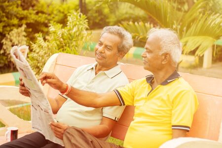 Two happy senior men reading newspaper at park outdoor - elderly friends enjoying moring news -...