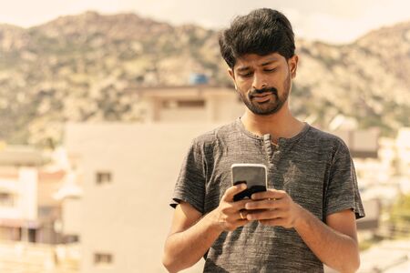 Young casual man busy in using a smart phone texting messages on terrace.の写真素材