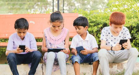 Children busy in using mobile phone at park - Concept of Kids on mobile devices and technology addiction - Young teens using technology, Internet on Smartphone.の写真素材