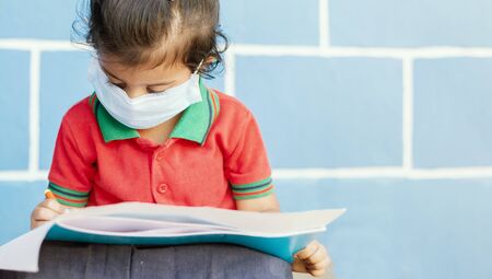 Covid 19 or Coronavirus and Air pollution pm2.5 concept - Little girl wearing medical mask and busy in writing at schoolの写真素材