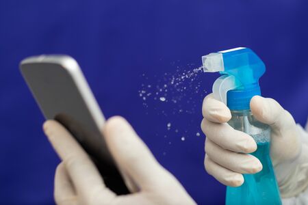 Doctor Cleaning mobile phone to eliminate Covid-19 - Nurse hands with gloves cleaning the phone by...