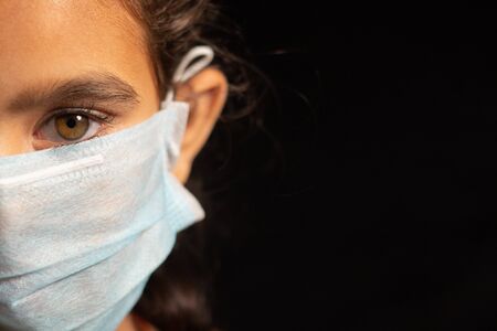 young girl child with medical mask wearing, protection against covid 19 or coronavirus pandemic on black background with copy space.の写真素材