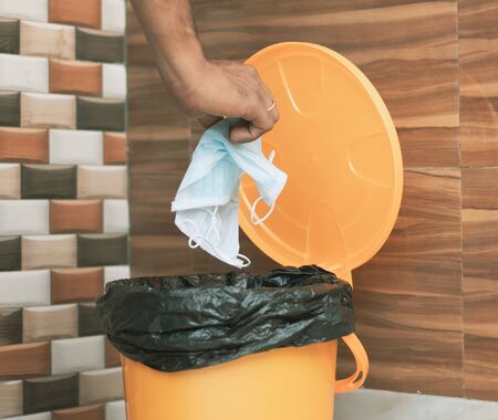 Hands throwing medical mask into closed bin - Covid-19, Coronavirus advice to discard or dispose medical mask to closed trash can after usage - concept showing to do hygiene practice.の写真素材