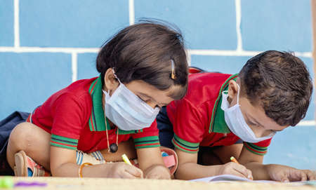 Kids busy in writing with medical face mask wearing due to covid-19 or coronavirus outbreak or...