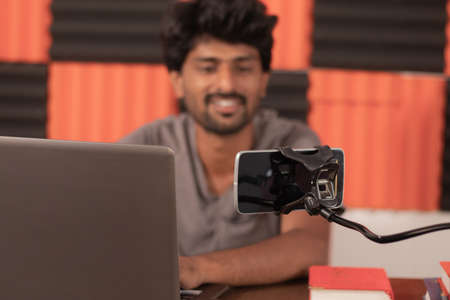 Young man looking on mobile busy in video chat with friends at home during  pandemic - Smiling...