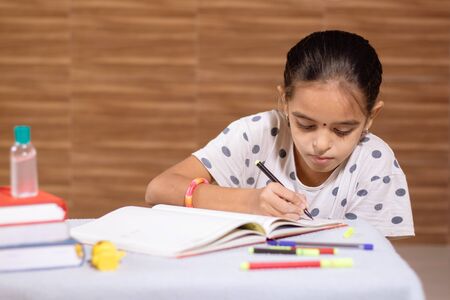 Little schoolgirl busy in doing homework with hand sanitizer in front during coronavirus or covid-19 outbreak - Concept of homeschooling, children educationの写真素材