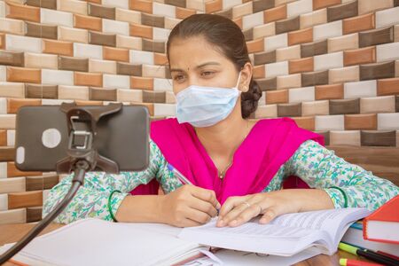 Concept of homeschooling and e-learning, College girl with medical mask listing virtual class on...