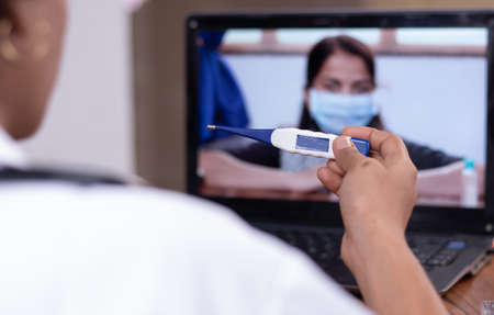 Doctor explaining how to use fever thermometer to patient through online on laptop - Concept of Online Chat, telehealth, or tele counseling with patient during coronavirus or covid-19 crisisの写真素材