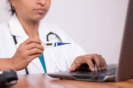 Doctor explaining how to use fever thermometer to patient through online on laptop - Concept of telehealth, or telemedicine with patient during coronavirus or covid-19 pandemic.の写真素材