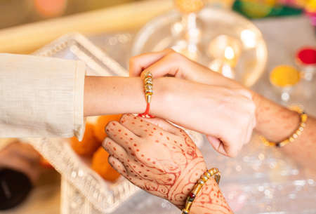 Closeup of hands, sister tying rakhi, Raksha bandhan to brothers wrist during festival or ceremony - Rakshabandhan celebrated across India as selfless love or relationship between brother and sisterの写真素材