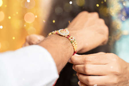 Closeup of hands, sister tying rakhi to brothers wrist during festivalの写真素材