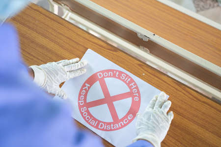 Shoulder shot of man with medical mask and hand gloves pasting dont sit here keep social distance...