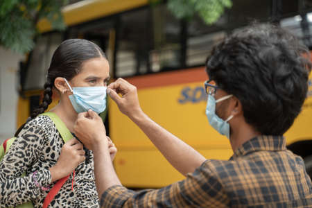 Father helping daughter to wear mask before getting inside the school bus as coronavirus or covid-19 safety measures - concept of back to school and new normal lifestyle.の写真素材