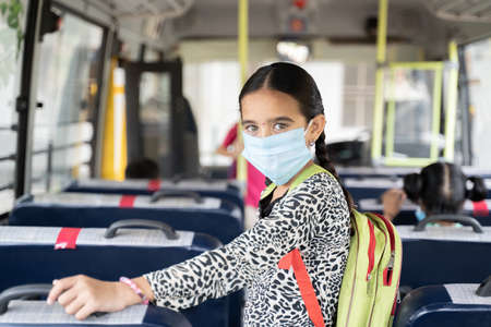 Portrait of Girl kid student in medical mask inside the school bus looking at camera - Concept of school reopen or back to school with new normal lifestyleの写真素材