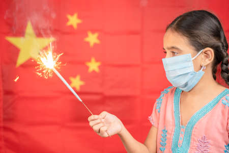 Young Girl Kid on medical mask holding Sparkler with Chinese flag as background - concept showing...