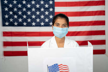 Doctor or nurse coming to polling booth with medical mask wearing for voting - concept of US...