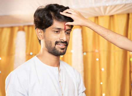 Close up Hands of Sister applying Tilak or mark to forehead of elder Brother during Bhai Dooj or...