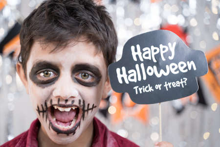 Kid hloding Halloween booth prop and making gesticulating spooky face - concept of halloween trick...