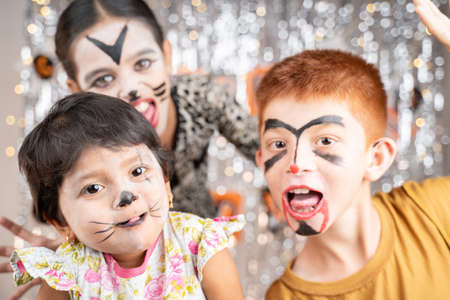 Group of kids in Halloween costumes gesticulating and making scary or spooky faces on decorated background by looking into camera.の写真素材