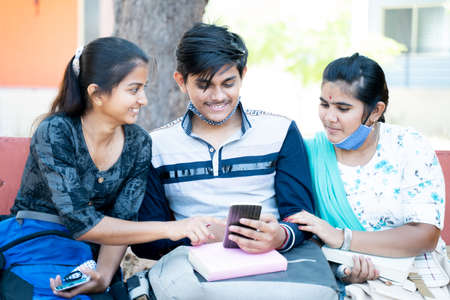 Three frinds while sitting at college laughing by looking into mobile phone - concept of students...