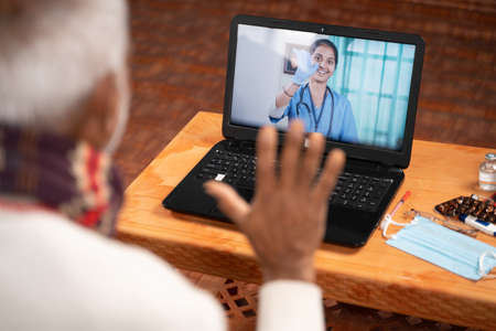 Shoulder shot of Old man on video with to doctor on laptop screen - concept of Online Chat, telehealth, or tele counseling with Nurse or Doctor during coronavirus or covid-19 pandemicの写真素材
