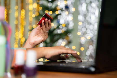 Concept showing of girl purchasing Cosmetic products online by holding card in hand and busy on laptop - Concept of holiday online shopping and e-commerce.の写真素材