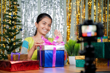Girl opening gift in front of camera during christmas eve - concept of vlogging, girl got gift or present from subscribers during holyday seasonの写真素材
