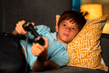 Alone young kid playing video game using joystick during late night while sleeping on bed - concept of kids game addiction and late night playing gamesの写真素材