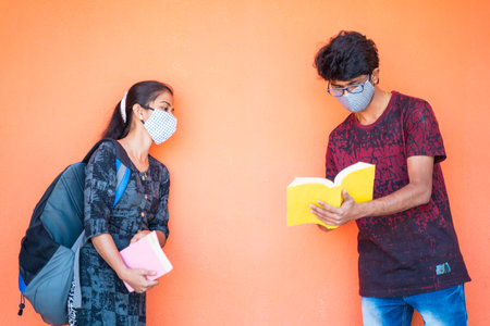Two students in face mask discussing at college while maintaining social distance - concept of...