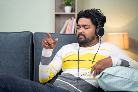 Young man listining peaceful music at home while lying on sofa - concept of music lover, lazy weekend relaxation and modern lifestyleの写真素材