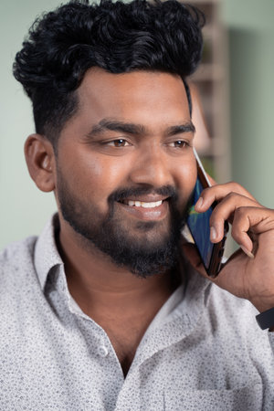 Close up of Smiling young Indian man busy talking or having conversation on mobile phone