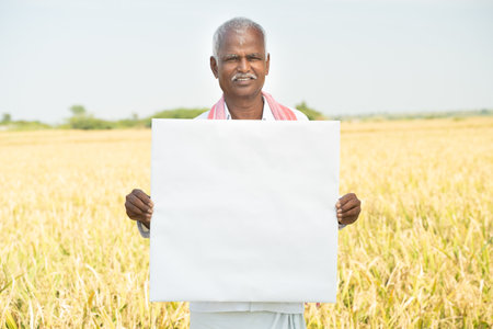 smiling Indian farmer Holding white card board or empty banner infornt of the agriculture farmlandの写真素材