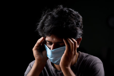 Young man with medical mask holding his head due to headache after receiving vaccine shotsの写真素材