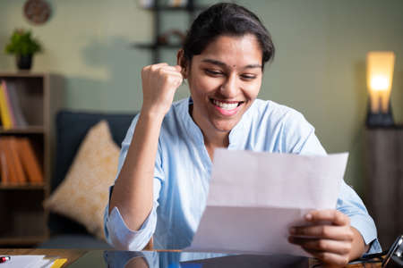 Young business woman reading paper letter feeling overjoyed and enjoying by good news clenched fist...