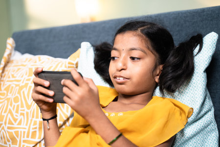 Young girl disabled kid using mobile phone while sleeping on sofa - concept of Kid mobile phone game addiction, technology and modern lifestyleの写真素材